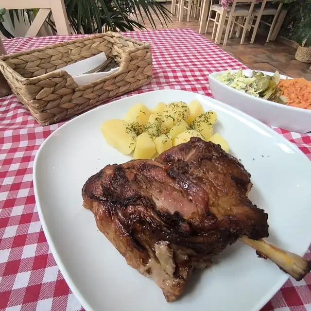 Pieczone mięso z kością, ziemniaki i surówki na obrusie w kratkę