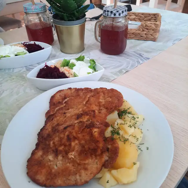 Panierowany kotlet z ziemniakami z koperkiem, obok surówki i dzbanek kompotu