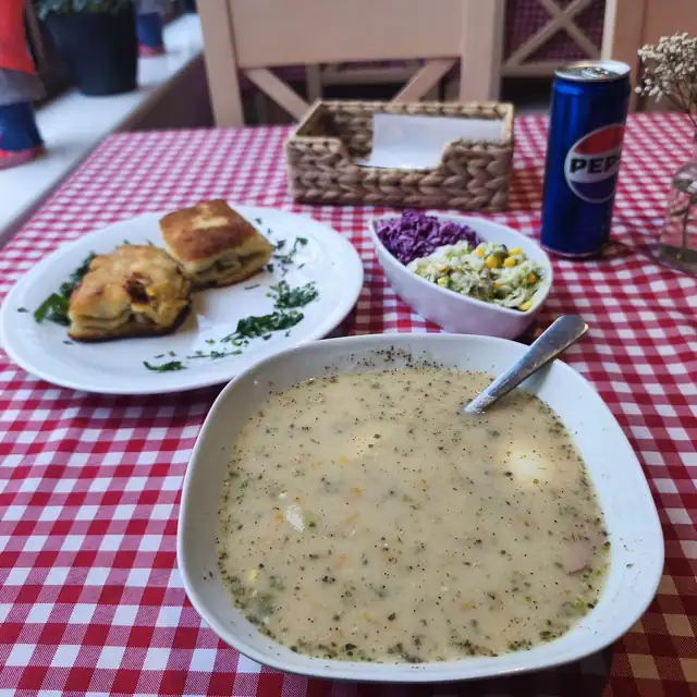 Talerz zupy i drugie danie na stoliku w kratkę, obok puszka napoju